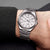 Reloj de hombre en la muñeca con esfera plateada y brazalete de metal plateado.
