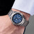 Pulsera de hombre en la muñeca con esfera azul, brazalete de metal plateado y corona