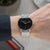"Reloj de hombre en la muñeca: esfera negra, manecillas rojas, correa de malla plateada"
