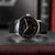 Reloj de hombre con esfera negra, segundero rojo y correa de cuero negra.
