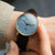 Reloj de mujer en la muñeca con esfera azul y correa de cuero marrón, caja dorada.
