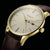 "Vista detallada del reloj unisex: esfera beige, corona dorada y correa de cuero marrón"