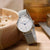 "Reloj de mujer en la muñeca con esfera blanca y correa de malla plateada"