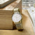 "Reloj de mujer sobre madera: esfera blanca y pulsera de malla dorada"