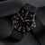 Reloj deportivo con correa negra, esfera negra y bisel rojo; fecha visible a las 3 en punto