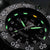 Primer plano de reloj para hombre: esfera negra con marcadores luminosos verdes y fecha