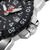Pulsera de hombre, vista lateral: caja de acero inoxidable con corona y bisel negro.