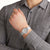 Reloj de pulsera en la muñeca: caja gris, esfera gris, correa textil gris.