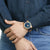Pulsera de reloj en la muñeca con esfera azul, bisel dorado y correa azul oscuro