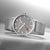 Reloj de hombre con correa de malla plateada y esfera gris, segundero rojo.