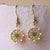 Pendientes dorados con detalle redondo verde y brillantes.