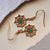 Pendientes con inserto redondo verde, diseño dorado y pedrería brillante.
