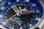 Primer plano: reloj de pulsera para hombre con esfera azul, manecillas grandes e índices plateados.