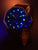 Pulsera de hombre con correa de cuero marrón; esfera azul con índices luminiscentes verdes.