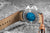 Pulsera de hombre con correa de cuero marrón; logo azul visible en la tapa trasera.