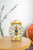 Reloj de mesa con campana de cristal dorada y números romanos sobre base redonda