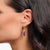 Pendientes de aro dorados con colgante de gota morada en la oreja