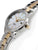 Reloj de mujer de perfil con caja plateada, pulsador dorado y brazalete bicolor.