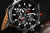 Reloj de pulsera para hombre con esfera negra, detalles en rojo y diseño de cronógrafo