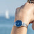 "Reloj de mujer en la muñeca con esfera azul, correa de metal plateado y manecillas"