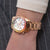 "Reloj de mujer en la muñeca, correa de metal dorado, esfera blanca y bisel multicolor"