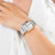"Reloj de mujer en la muñeca con pulsera de metal plateado y caja cuadrada"