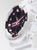 "Reloj de mujer de perfil: caja blanca, esfera negra con detalles en rosa"