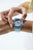 "Reloj de mujer en la muñeca, pulsera transparente turquesa y caja gris"