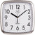 Reloj de pared cuadrado con esfera blanca, manecillas y números negros, logo JVD