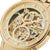 Reloj de hombre dorado con esfera esqueleto, índices en el borde de la caja
