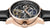 Reloj de hombre con bisel de oro rosa, movimiento automático visible y correa de cuero negra