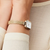 Reloj de mujer en la muñeca con correa milanesa dorada y esfera blanca.