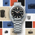 Reloj de hombre con correa de acero inoxidable plateado y esfera negra, ventana de fecha "LUN 6".