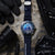 Reloj de buceo con esfera azul y correa de caucho azul oscuro sobre superficie mojada