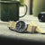 Reloj de hombre con correa de tela beige, esfera negra y caja redonda plateada