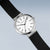 "Reloj de mujer en vista lateral: correa de cuero negra, caja plateada, esfera blanca"