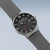 Reloj solar para hombre con esfera negra, detalles naranjas y correa de milanesa