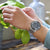 Reloj de hombre en la muñeca con esfera azul, correa de metal y manecillas luminosas