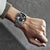 Reloj de pulsera de acero inoxidable con esfera negra, cronógrafo y brazalete de acero plateado.