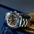 Reloj de hombre con correa de metal, esfera negra de cronógrafo y bisel azul de taquímetro