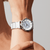 "Reloj de mujer en la muñeca con esfera blanca y brazalete de cerámica plateada."