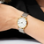 "Reloj de mujer en la muñeca con correa de metal plateado, caja dorada y esfera blanca"