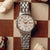 "Reloj de mujer con pulsera de acero inoxidable plateado, esfera clara y corona dorada"