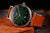 Reloj de hombre con correa de cuero marrón, caja plateada y esfera verde oscuro, logo Bauhaus
