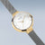"Reloj de mujer con caja redonda dorada, esfera blanca y correa de malla gris"