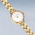 Reloj de mujer en tono dorado, vista cercana de la esfera con índices y manecillas, y brazalete de eslabones.