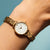 Reloj de mujer en la muñeca con pulsera de eslabones dorados y esfera blanca.