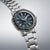 Reloj de hombre con esfera azul, manecilla GMT, brazalete de metal y corona estriada