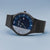 Reloj de hombre frontal en ángulo: esfera azul, bisel negro, correa de malla negra