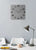 Reloj de pared cuadrado en la pared con esfera gris y números plateados.